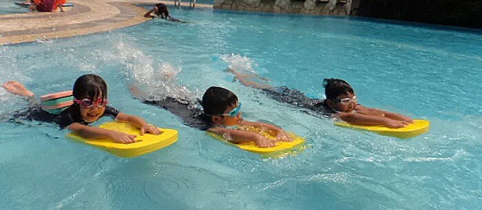 3 kids learning to swim with a floating board