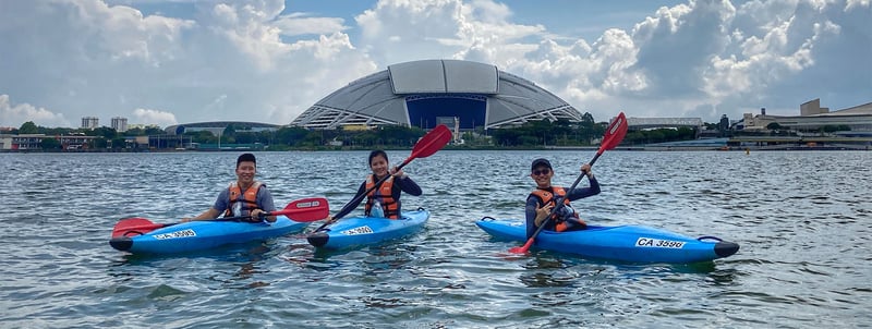 3 paddlers kayaking in front of the national stadium